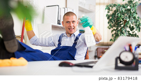 Relaxed cleaning service worker sitting in office with feet on table 83179418