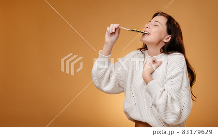 Woman enjoying biting green candy on yellow background. 83179629