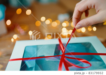 Close-up of woman's hand pulling ribbon from gift box. 83179932