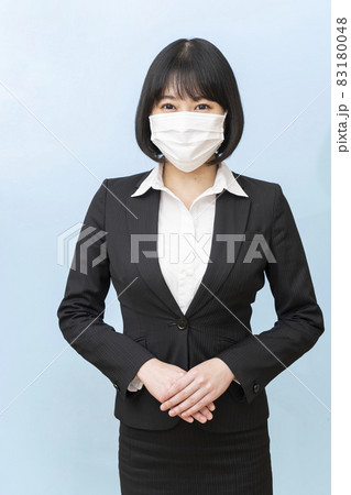 スーツ姿で不織布のマスクをして青い壁の前に立つ若い女性 83180048