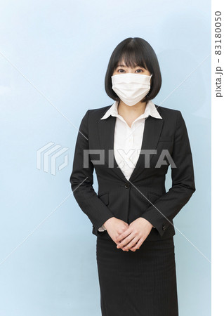 スーツ姿で不織布のマスクをして青い壁の前に立つ若い女性 スーツ姿で不織布のマスクをして青い壁の前に立つ若い女性 83180050