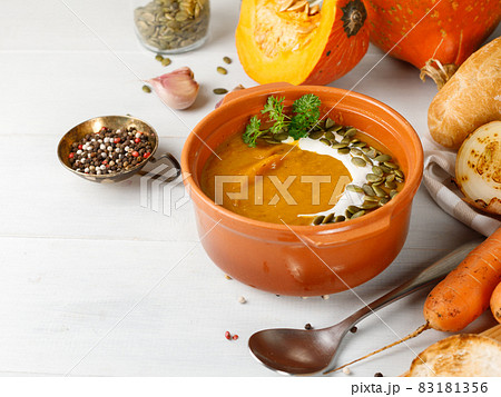 Thick pumpkin soup in a ceramic bowl. On a light wooden table with ingredients for cooking. Close-up, copy of the space 83181356
