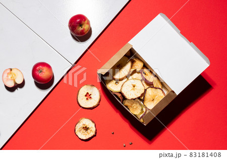 Apple chips in a cardboard container. Top view on contrasting red and white background Apple chips in a cardboard container. Top view on contrasting red and white background 83181408