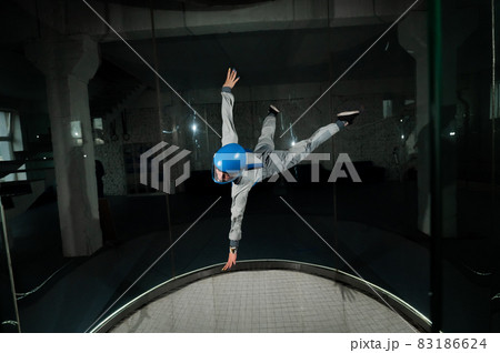 A young woman in overalls and a protective helmet enjoys flying in a wind tunnel. Free fall simulator A young woman in overalls and a protective helmet enjoys flying in a wind tunnel. Free fall simulator 83186624
