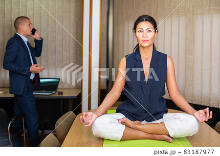 Relaxed businesswoman sitting in lotus position on desk in office Relaxed businesswoman sitting in lotus position on desk in office 83187977