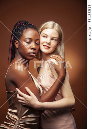 two pretty girls african and caucasian blond posing cheerful together on brown background, etnithity diverse lifestyle people concept two pretty girls african and caucasian blond posing cheerful together on brown background, etnithity diverse lifestyle people concept 83188913