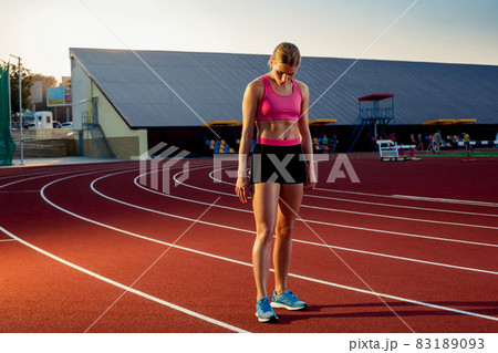 Picture of beautiful young European female runner or sprinter standing on outdoor stadium track, feeling exhausted after sprint or marathon. Picture of beautiful young European female runner or sprinter standing on outdoor stadium track, feeling exhausted after sprint or marathon. 83189093