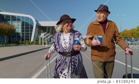 Senior pensioner tourists grandmother grandfather stay from airport hall with luggage on wheels 83190243
