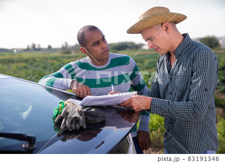 Two farmers discussing papers near car on field 83191346