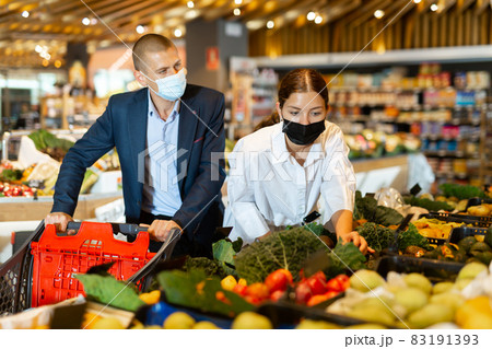 Young couple wearing protective masks in the supermarket chooses avocados 83191393