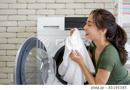 Asian housewife inhaled the smell of white cloth that was just washed from the washing machine. Working atmosphere in the laundry room. Asian housewife inhaled the smell of white cloth that was just washed from the washing machine. Working atmosphere in the laundry room. 83195385