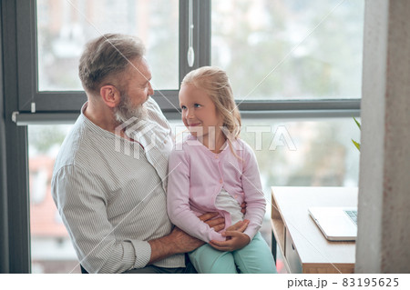 A businessman sitting at the table and holding his small daughter A businessman sitting at the table and holding his small daughter 83195625