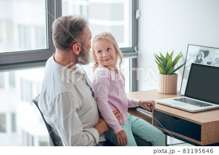 A businessman sitting at the table and holding his small daughter 83195646
