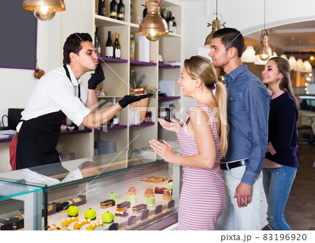 Two women and man are choosing delicious cakes from showcase 83196920
