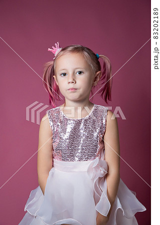 Little caucasian girl in a festive dress with sequins posing on a pink backgdrop Little caucasian girl in a festive dress with sequins posing on a pink backgdrop 83202189