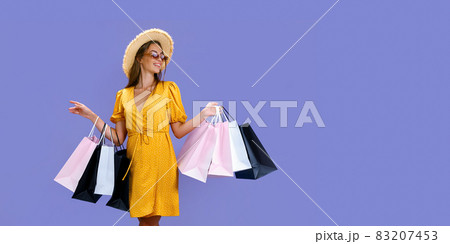 Pretty woman in sunglasses and hat holds colourful shopping bags on purple background. Sales concept Pretty woman in sunglasses and hat holds colourful shopping bags on purple background. Sales concept 83207453