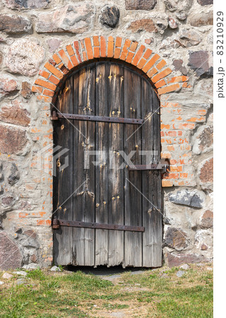 Old arched wooden door in a stone wall 83210929