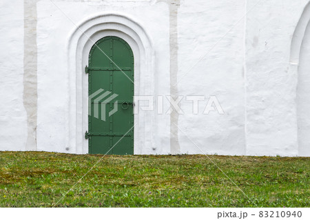 Closed green door in an old white stone wall 83210940