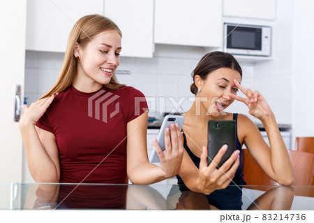 Two young girlfriends making selfie by phone and smiling at table 83214736