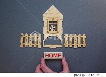 Model of a wooden house. Word 'home' on wooden block. Male hand, wooden fence. Copy space. Business concept. Beautiful grey background. Model of a wooden house. Word 'home' on wooden block. Male hand, wooden fence. Copy space. Business concept. Beautiful grey background. 83219466