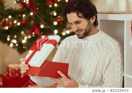 Man With Present in the Gift Box Near Christmas Tree at Home Man With Present in the Gift Box Near Christmas Tree at Home 83220453