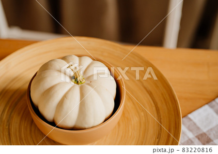 a small decorative white pumpkin in a clay bowl on a wooden platter. 83220816