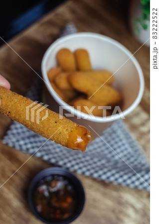 Cheese sticks in a female hand. A large portion of fast food in batter, which lies in a disposable container. Paper bucket for food delivery. Concept of restaurants and fast food cafes Cheese sticks in a female hand. A large portion of fast food in batter, which lies in a disposable container. Paper bucket for food delivery. Concept of restaurants and fast food cafes 83222522
