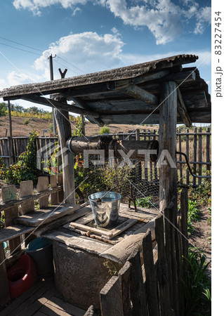 Old wooden draw well. Tin bucket. Countryside landscape Old wooden draw well. Tin bucket. Countryside landscape 83227454