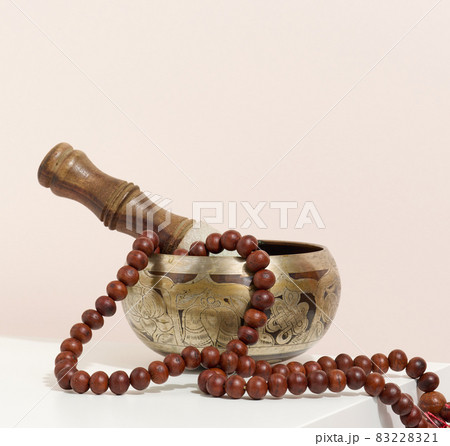 copper singing bowl and wooden clapper on a white table. Musical instrument for meditation, relaxation, various medical practices related to biorhythms, normalization of mental health 83228321