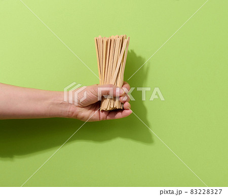 female hand holds disposable wooden sticks for stirring hot drinks on a green background. Coffee and tea spoon female hand holds disposable wooden sticks for stirring hot drinks on a green background. Coffee and tea spoon 83228327