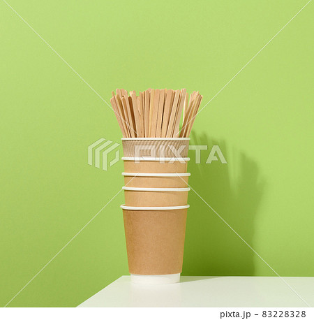 brown paper cardboard cups and wooden stirring sticks on a white table, green background. brown paper cardboard cups and wooden stirring sticks on a white table, green background. 83228328