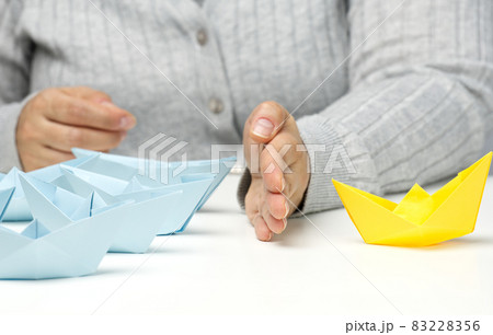 paper boats between a female hand on a white table. Conflict solution concept, negotiator between groups. Searching of decisions 83228356