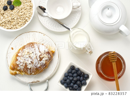 Raw oatmeal in white ceramic plate, blueberry, honey on white table, breakfast 83228357