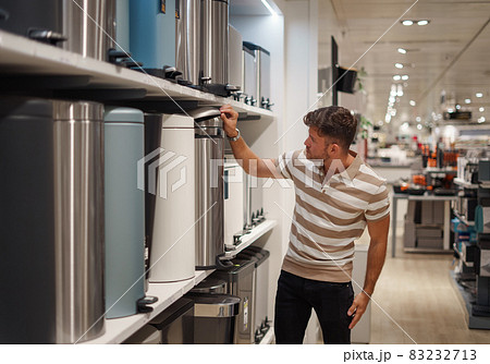 Male client in casual clothes opening lid of modern rubbish bin placed on shelf in mall 83232713