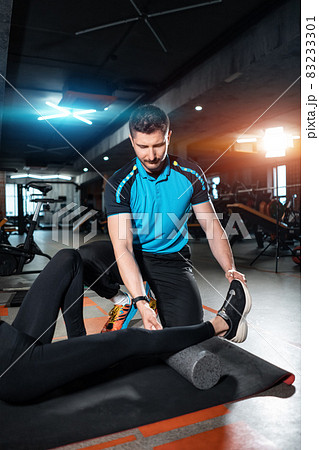 young female relaxing with myofascial release roller with trainer in gym 83233301