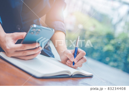 Business woman hand writing on a notepad with a pen and she is holding a cell phone in the office. Business woman hand writing on a notepad with a pen and she is holding a cell phone in the office. 83234408