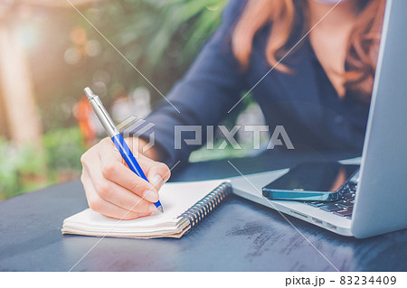 Business woman hand writing on a notepad with a pen in the office.On the table was a cell phone and a laptop computer. 83234409