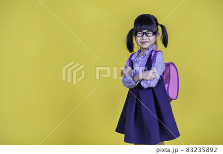 Portrait of young happy little cute asian girl in school uniform isolated on yellow background with copy space. Education for toddler or preschool, childhood lifestyle back to school concept Portrait of young happy little cute asian girl in school uniform isolated on yellow background with copy space. Education for toddler or preschool, childhood lifestyle back to school concept 83235892