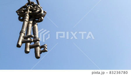 Three old vintage antique rust keys hang in the foreground against a blue sky 83236780