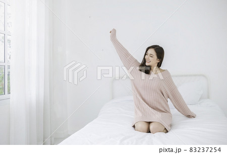 Portrait of young beautiful sexy asian woman relax stretching in bedroom. Smile happy face asian girl look up on white certain. Beauty treatment perfect clear skin makeup winter lifestyle concept 83237254