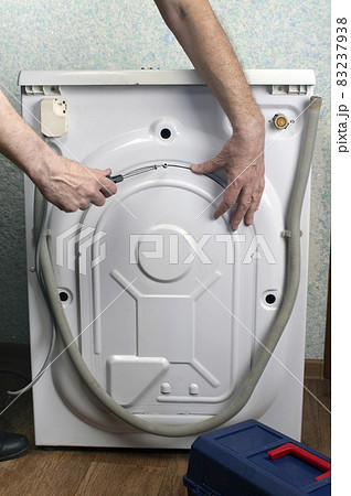 Washing machine repair. A man screws the back of a washing machine with a screwdriver. Repair of large household appliances Washing machine repair. A man screws the back of a washing machine with a screwdriver. Repair of large household appliances 83237938