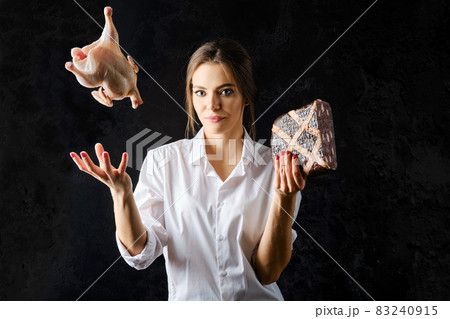Woman tossing up fresg chicken with one hand and holding meat pie with another Woman tossing up fresg chicken with one hand and holding meat pie with another 83240915