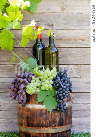 Various colorful grapes and wine bottles on wine barrel Various colorful grapes and wine bottles on wine barrel 83244568