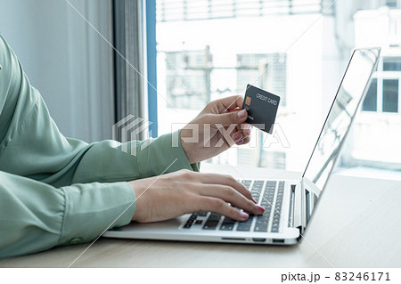 The businesswoman's hand is holding a credit card and using a laptop for online shopping and internet payment in the office 83246171