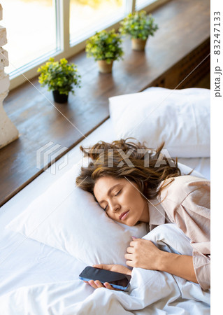Vertical photo of a sleeping woman with smartphone in bed - digital addiction concept. 83247133