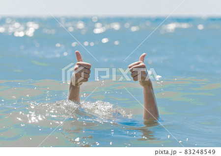 Hands from under the water of a drowning girl shows class with a thumb up. Help and urgent rescue of a person during a dangerous swimming, sos 83248549