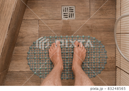 Men's feet stand on a plastic anti-slip mat next to the floor drain in the bathroom or shower 83248565