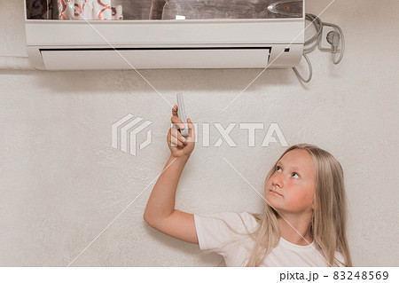 Young girl cute blonde teenager of European appearance holds in his hands a remote control of air conditioning in the interior of the room Young girl cute blonde teenager of European appearance holds in his hands a remote control of air conditioning in the interior of the room 83248569