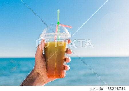 The guy's hand holds a colored chilled non-alcoholic cocktail against the background of the sea 83248751