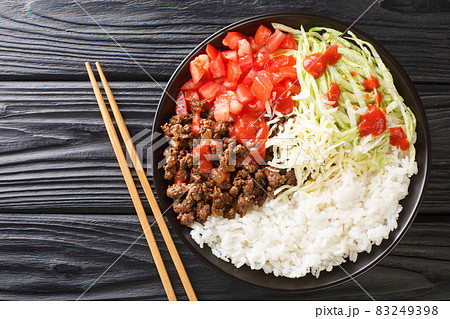 Taco rice takoraisu is a Mexican Japanese fusion dish consisting of seasoned ground beef, shredded lettuce, and chopped tomatoes served over a bed of white rice close-up. Horizontal top view 83249398